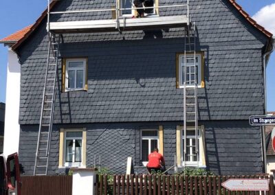 Ein Mann streicht ein Haus mit einer Leiter.