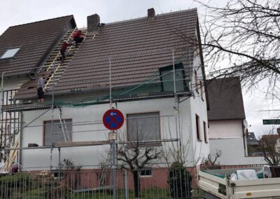 Ein Mann arbeitet an einem Dach vor einem Haus.